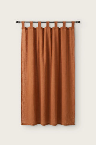 Stonewashed cotton curtain panel in terracotta, single tab top panel on a black rod, front view
