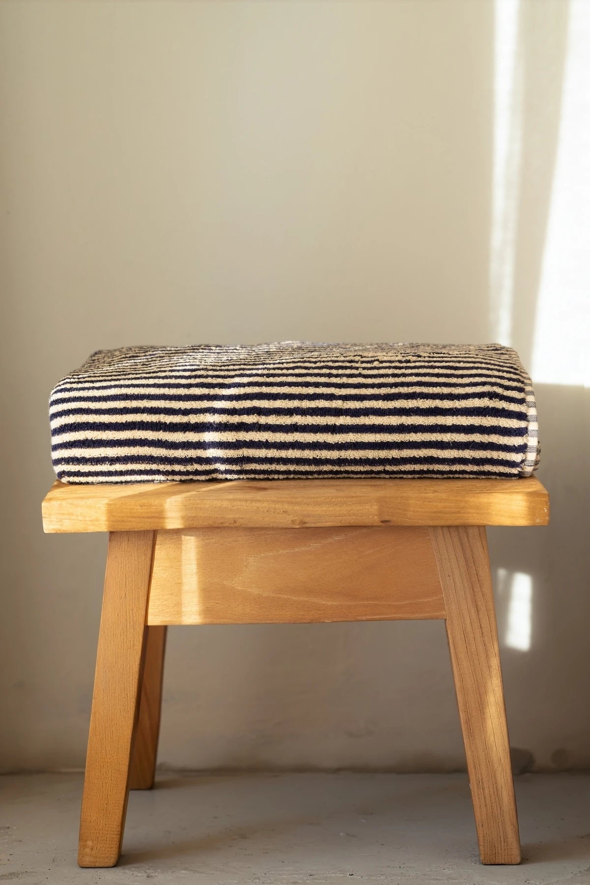 Navy striped Turkish cotton bath sheet folded on a wooden stool - VivaMaison