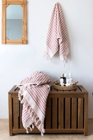 Pink Turkish cotton pom pom towel in a bathroom, hanging and draped over a wooden chest - VivaMaison
