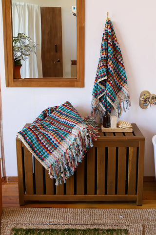 Rainbow Turkish cotton pom pom towel in a bathroom, hanging and draped over a wooden chest - VivaMaison